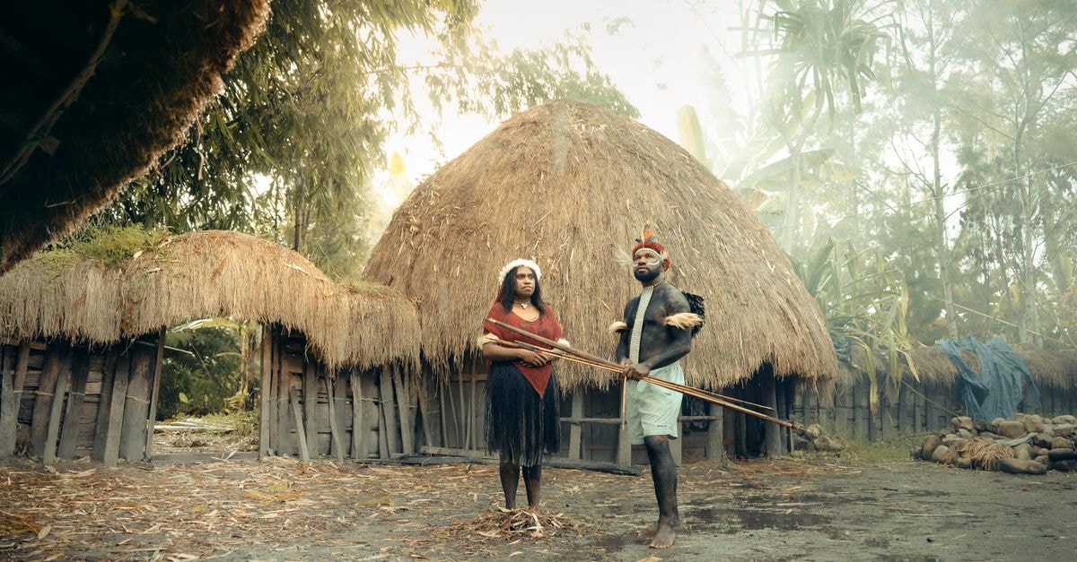 Nzérékoré Travel Guide: Into Guinea's Forest Heart Two indigenous people in traditional attire stand in front of a thatched hut in Papua New Guinea.
