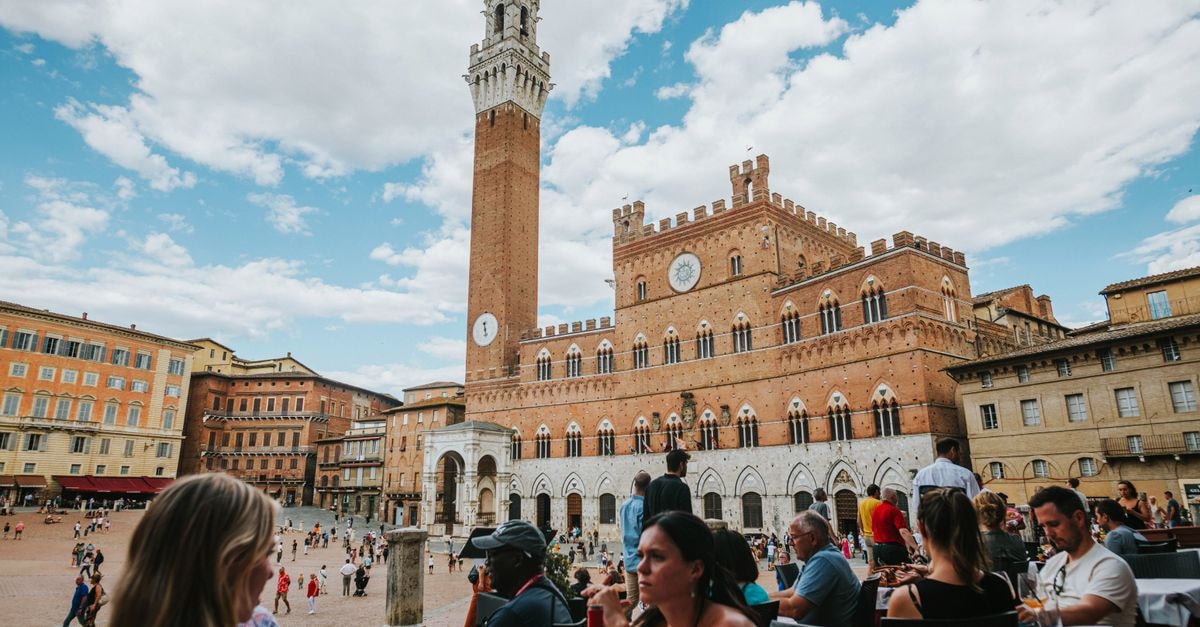 I Terzi di Siena in Siena: Rooftop Views Over the Medieval Skyline Lively scene at Piazza del Campo, Siena with Torre del Mangia and people enjoying dining outdoors.