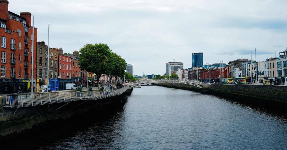 Scenic view of Dublin's Ha'penny Bridge over the River Liffey amidst urban architecture and vibrant city life.