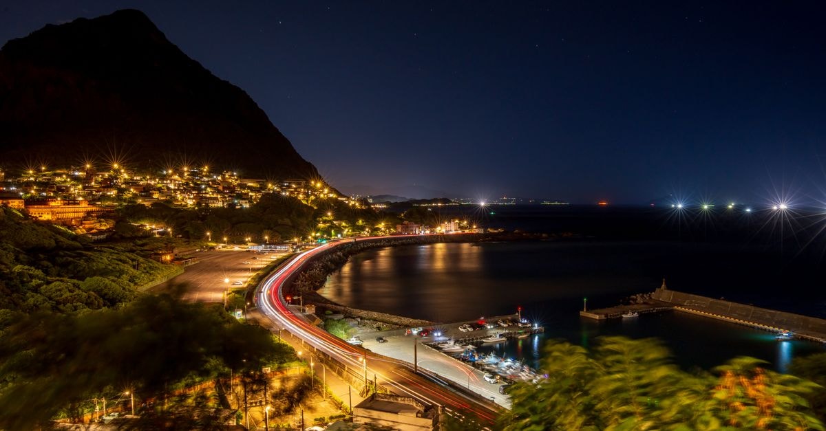 Stunning night view of a coastal road and urban lights reflecting on the water.