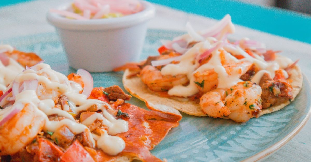 Ensenada Travel Guide: Harbor Light and Slow Tostadas Tasty shrimp tacos topped with creamy sauce and fresh onions on a ceramic plate.