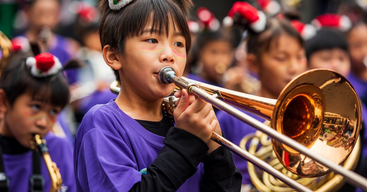 Chiayi Petite Hostel in Chiayi City: An Old-House Stay on Linsen West Road Child playing trombone in a festive parade, wearing a holiday hat, outdoors.