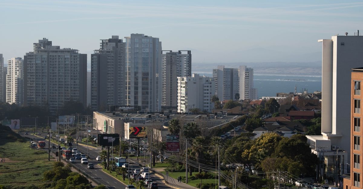 Aerial city view featuring tall buildings and a distant coastline under a clear blue sky.