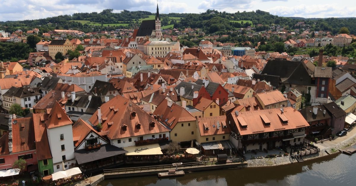 Aerial view of Český Krumlov showcasing picturesque red rooftops by the river under a cloudy sky.
