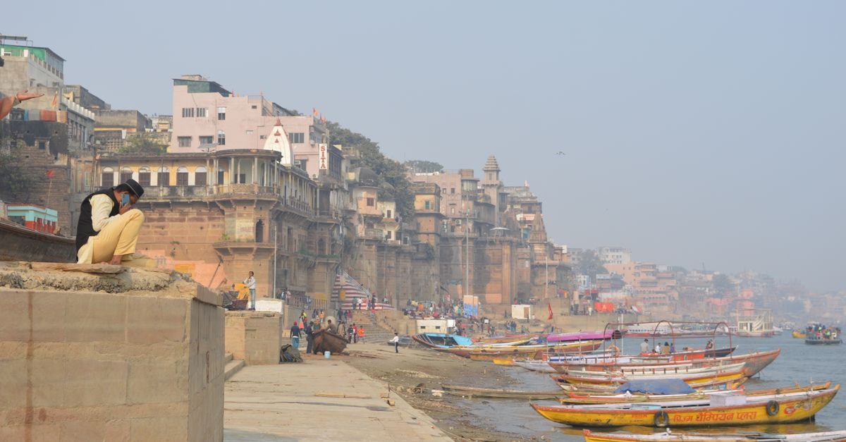 Hotel Alka, Varanasi — A Ghat-Side Stay on Tripura Bhairwi Colorful boats docked on the Ganges River, with historic Varanasi ghats and architecture in the background.