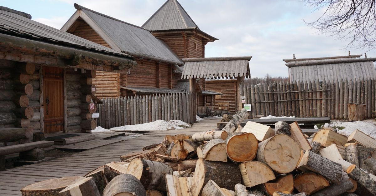 Nizhny Novgorod Travel Guide: Planning Tips, Costs and Things to Do Chopped logs piled in front of traditional Russian wooden buildings, showcasing rustic architecture.