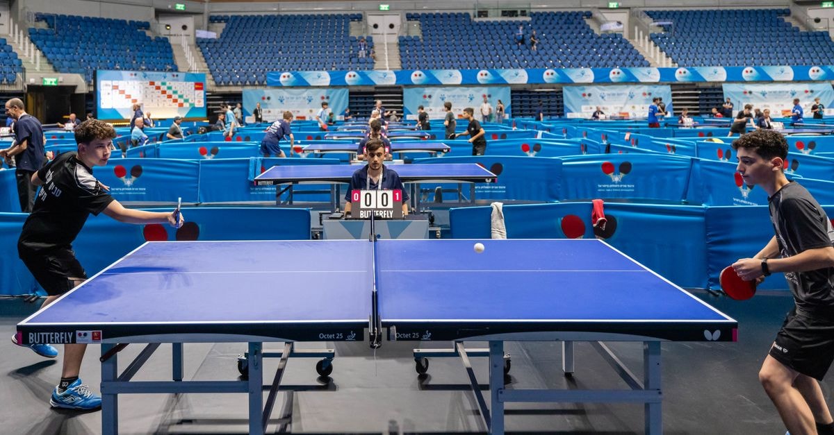 Players compete in a lively table tennis tournament in a large indoor stadium.