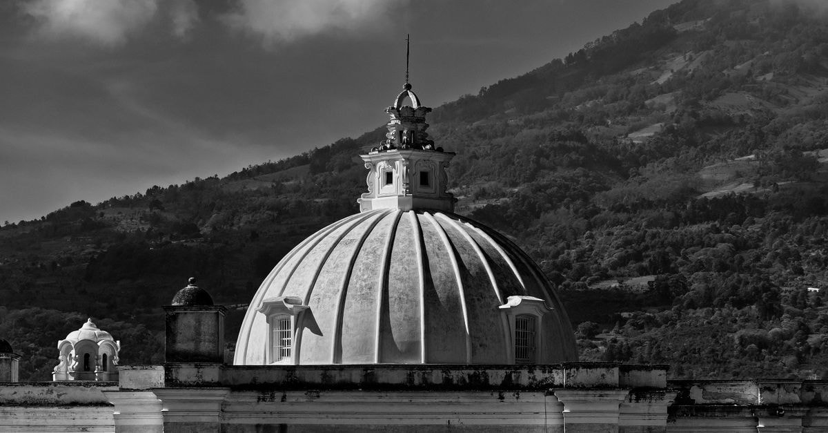 Hotel La Catedral, Antigua Guatemala — Steps From Central Park Grayscale photo of a historic dome with a scenic mountain backdrop in Antigua, Guatemala.