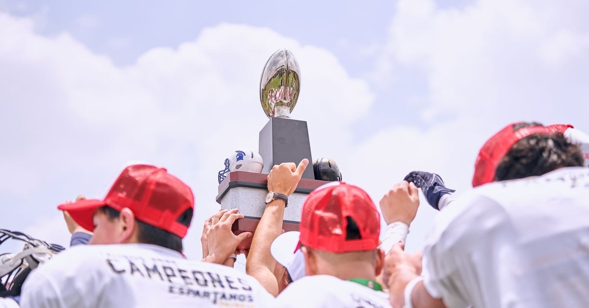 Harbaugh Era Opens With Giants' 28-20 Win Over Cowboys Group of athletes lifting a championship trophy outdoors in celebration.