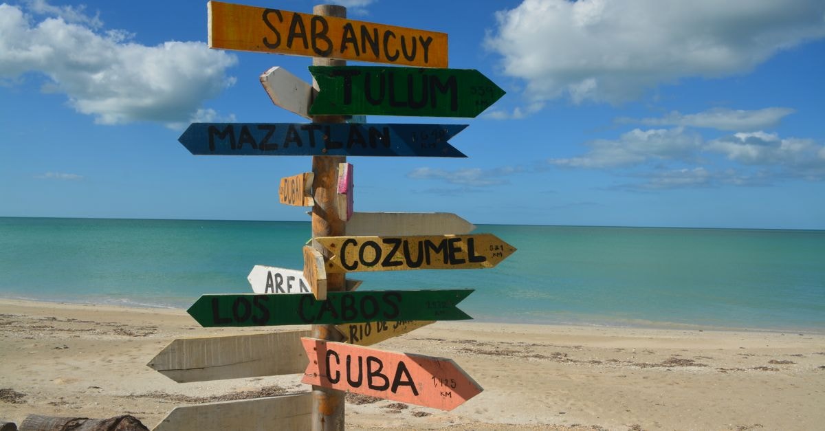 Punta Cana Travel Guide: Beaches, Resorts, and Getting Around Colorful signpost on a sunny beach, pointing to popular vacation destinations.