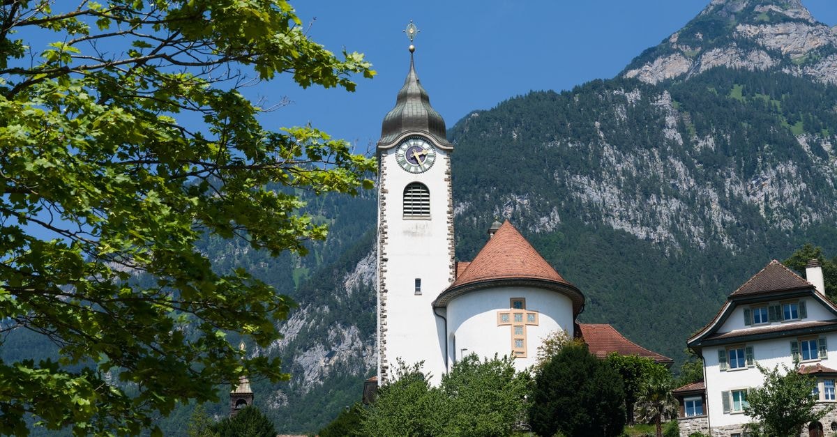 Scenic view of a church in Glarus, Switzerland, with lush greenery and Alpine mountains in the background.