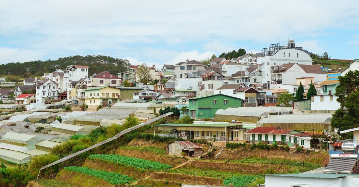 Muong Thanh Holiday Da Lat Hotel in Da Lat: A Lakefront Address in the City Center Idyllic rural village with greenhouses and houses nestled on a hillside under a bright sky.