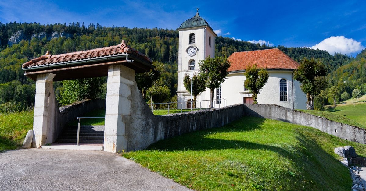A picturesque Swiss church nestled in a lush valley against a mountain backdrop on a clear summer day.