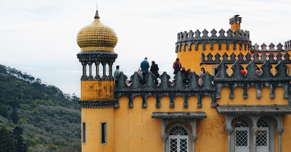 Colorful yellow towers of Pena Palace in Sintra, Portugal with visitors exploring its historic architecture.