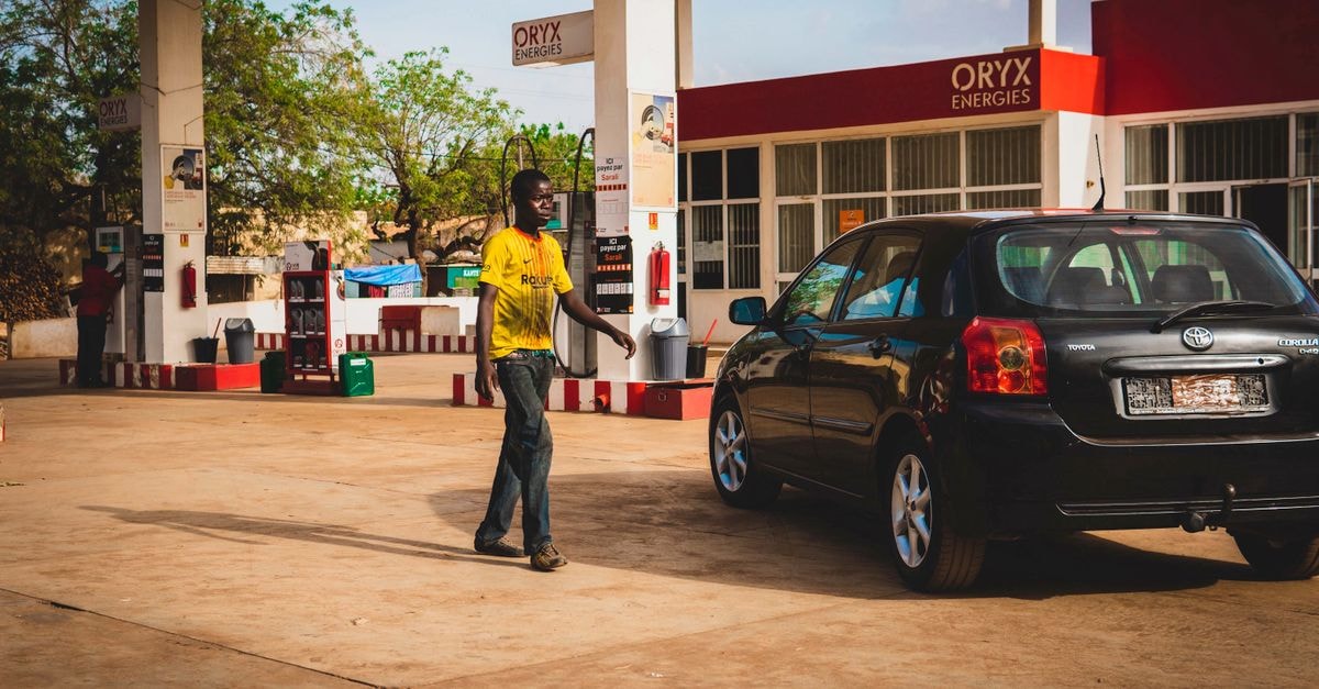 Ndele Travel Guide: Quiet Northern CAR Beyond the Map Man at a gas station fueling a black car under the bright daylight.