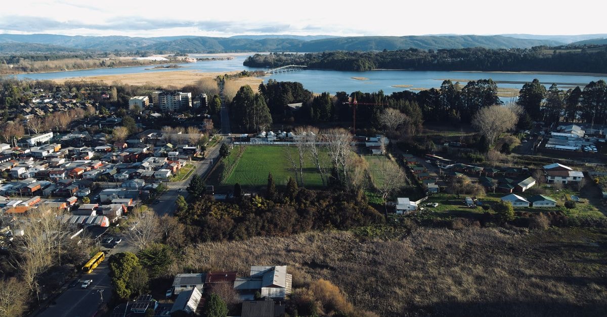 Hostal del Muelle in Valdivia: Steps from the Waterfront Aerial panoramic view featuring a city, lush forests, and a serene lake.