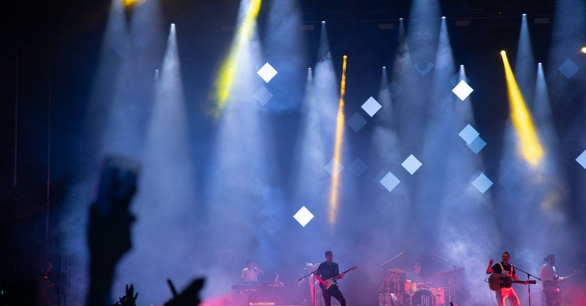Energetic live performance featuring a band on stage under vibrant lights and smoke effects.