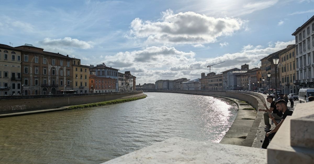 NH Pisa in Pisa: Right Across From the Central Station Picturesque view of the Arno River flanked by historic buildings in Pisa, Italy, under a sunny sky.
