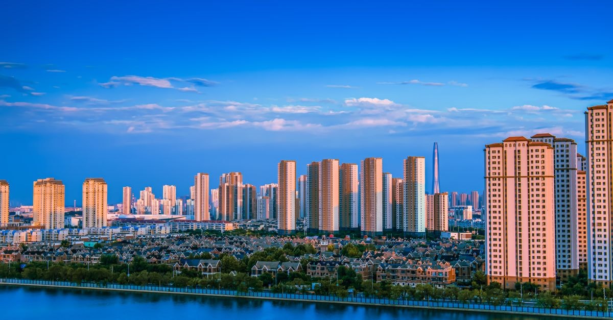 Baishan Hotel, Yanji — A Bukharton River Address with 1988 Roots Stunning view of a modern city skyline reflecting on a tranquil waterfront under a blue sky.