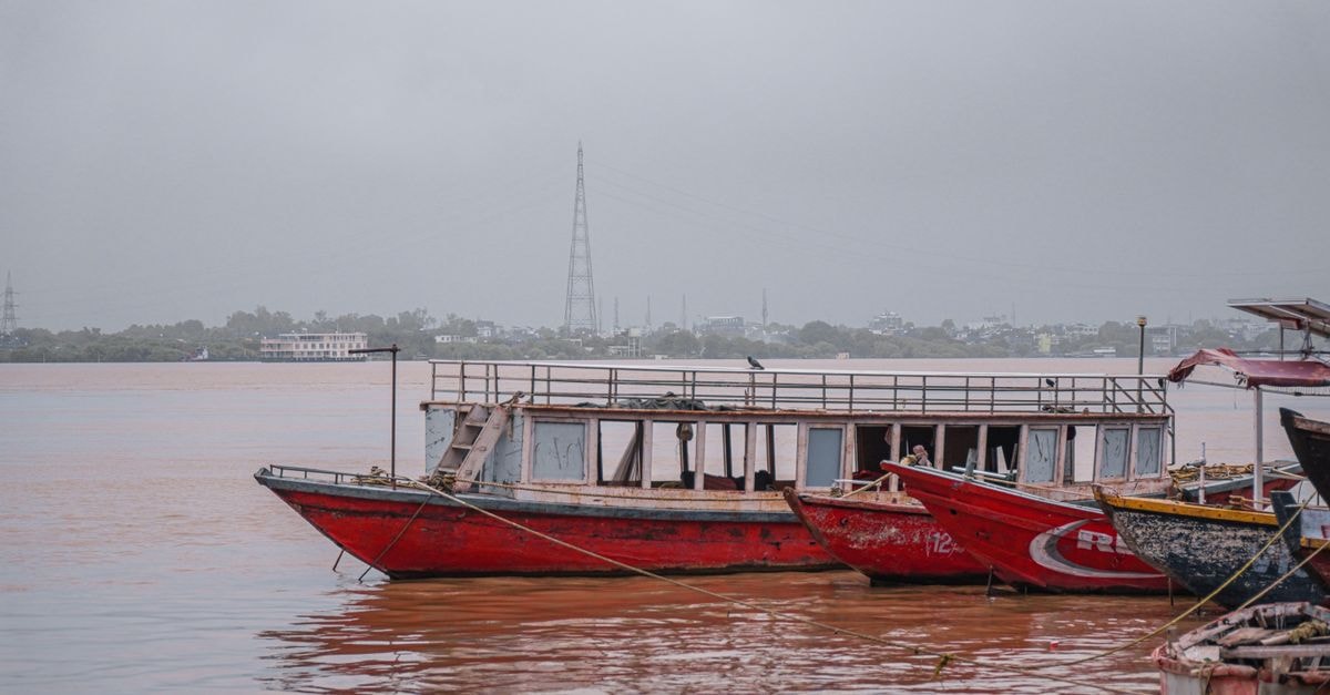 Garissa travel guide: riverfront culture on Kenya's eastern edge Red boats anchored on a tranquil river under an overcast sky, evoking serene and moody vibes.