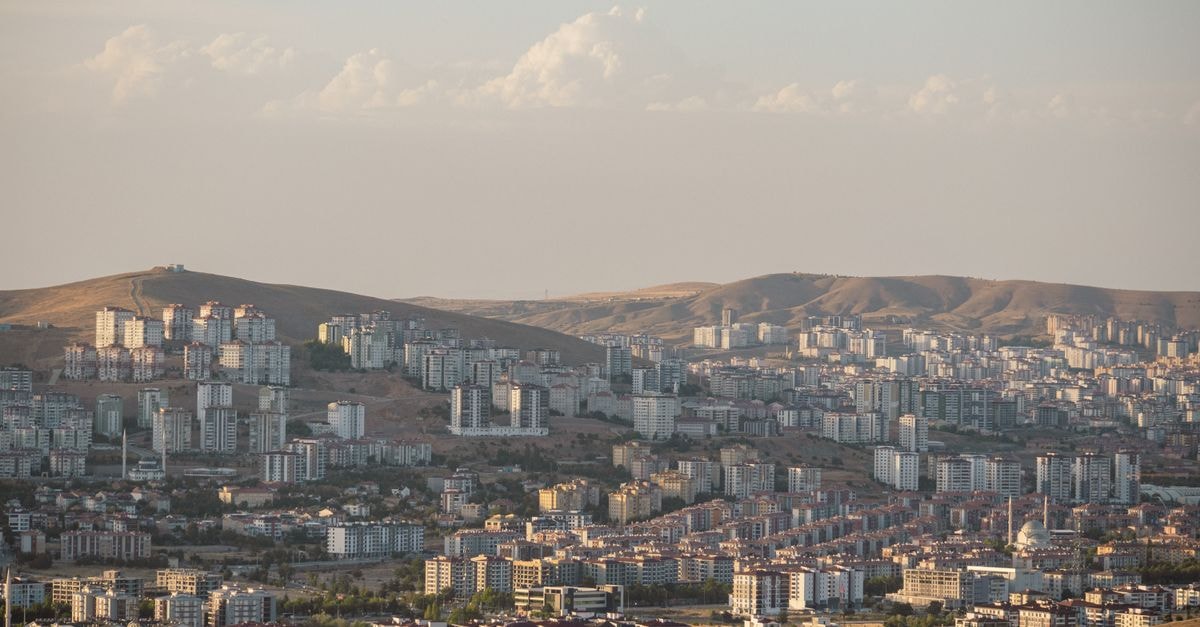 A panoramic cityscape showcasing urban buildings nestled in a hilly terrain under a sunset sky.