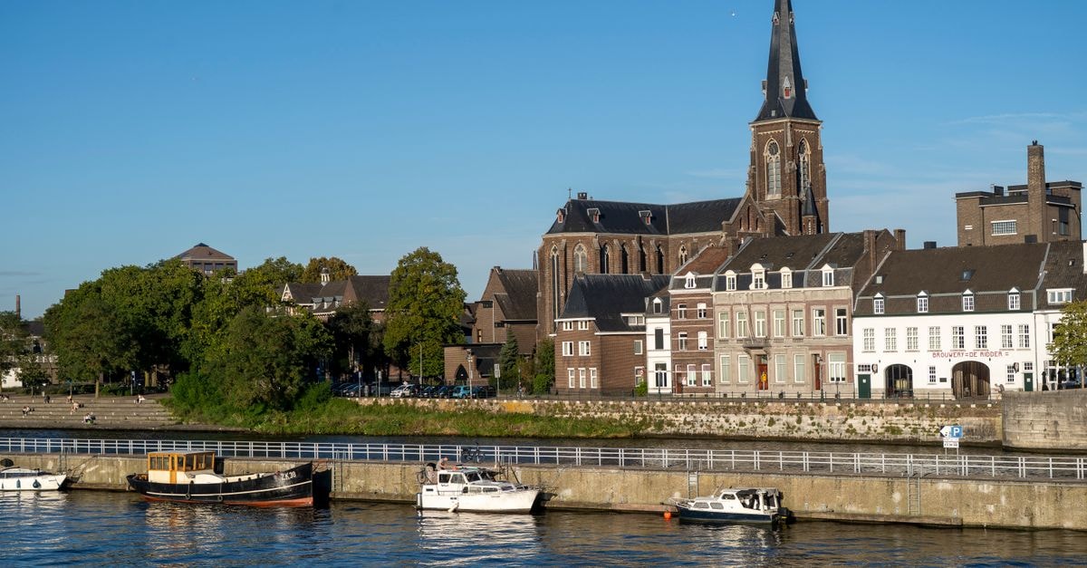 Bastion Hotel Maastricht Centrum, Maastricht — Right in the Historic Heart Discover Maastricht's charming riverside with historic buildings and the iconic church under a bright summer sky.
