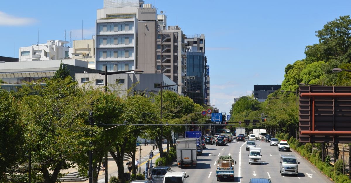 A vibrant city scene showcasing traffic on a busy road lined with buildings and greenery on a clear day.