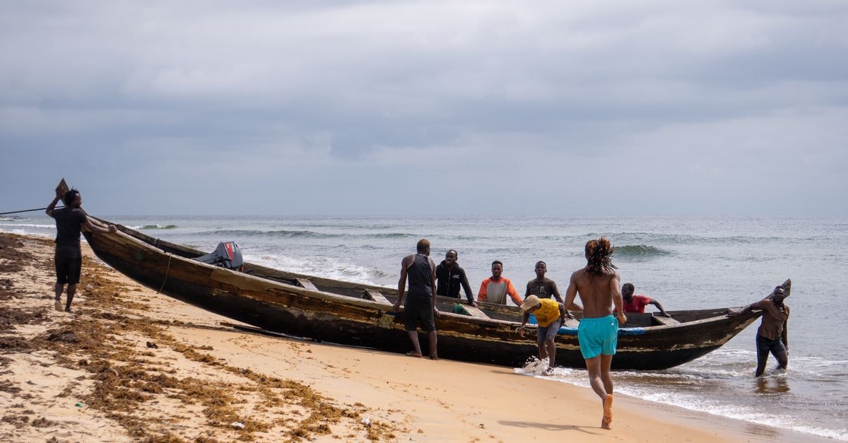 Buchanan, Liberia: a slow-paced coastal city travel guide Fishermen haul a wooden boat onto a sandy beach under a cloudy sky.
