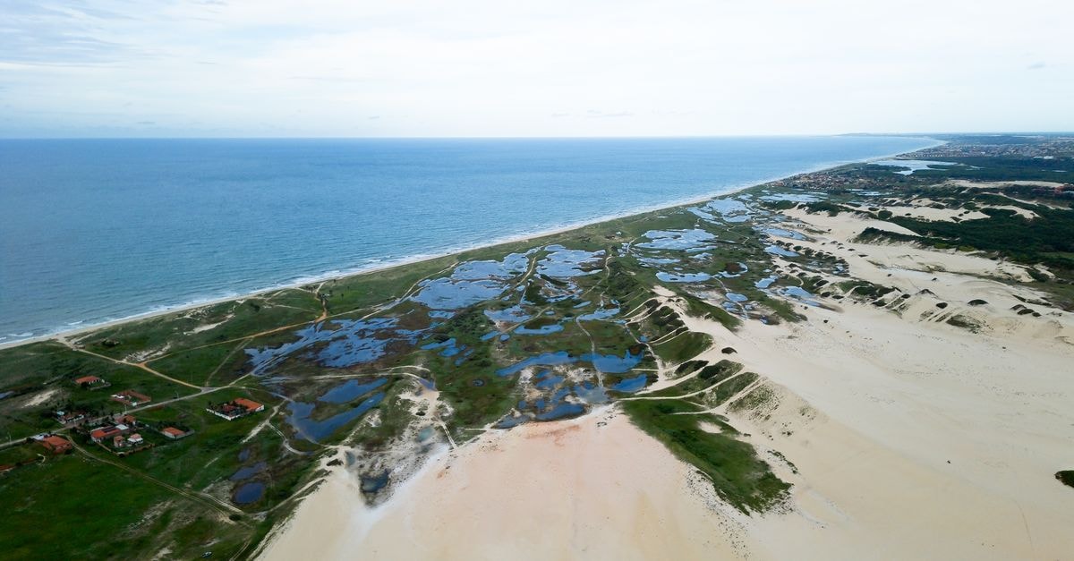 Drone captures expansive sand dunes and ocean in Fortaleza, Brazil, showcasing nature's beauty.