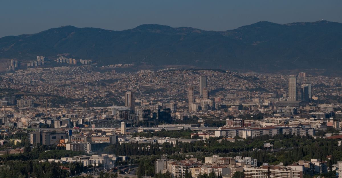Aerial view of Izmir, Türkiye, showcasing cityscape and mountainous backdrop under a clear blue sky.
