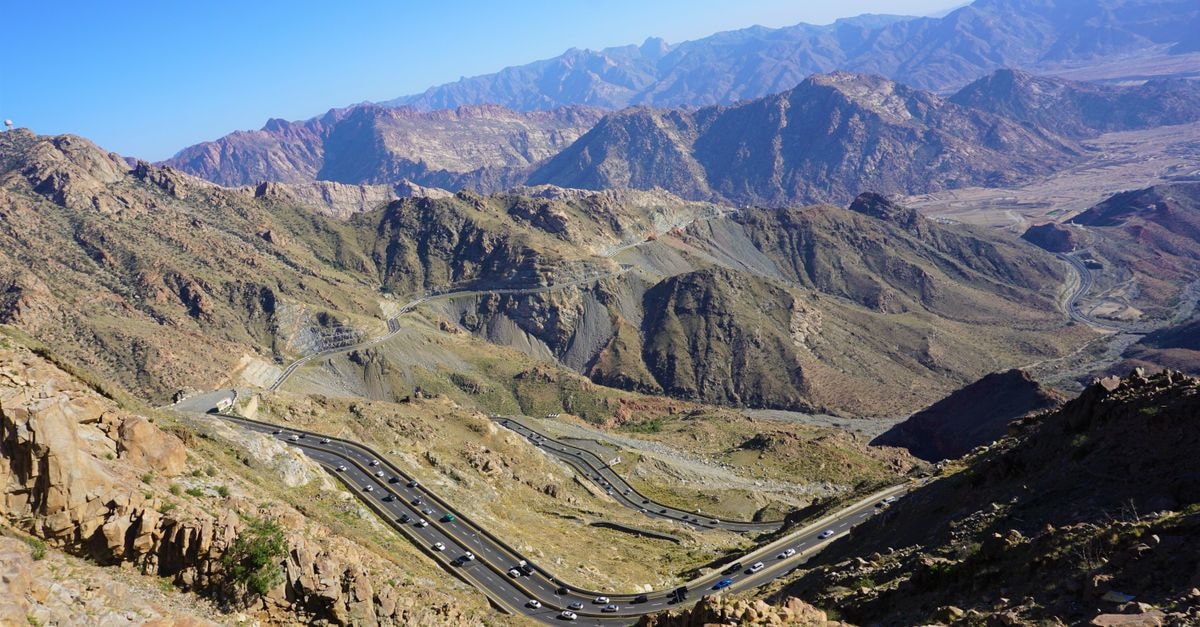 A breathtaking aerial shot of winding roads through majestic mountains under a clear blue sky.