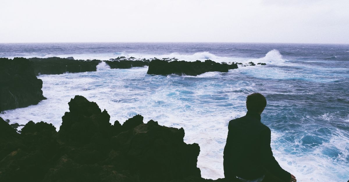 Hotel do Colégio in Ponta Delgada: A 19th-Century Manor with Music Still in the Walls A person sits on rocky cliffs in Azores, Portugal, gazing at the turbulent Atlantic Ocean under a cloudy sky.