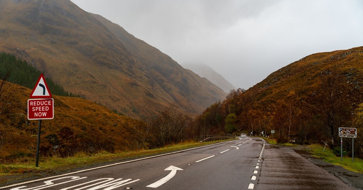 Malang Travel Guide: A Cool Highland City Worth Slowing Down For A winding road in the Scottish Highlands during autumn with a reduce speed sign and foggy mountains.