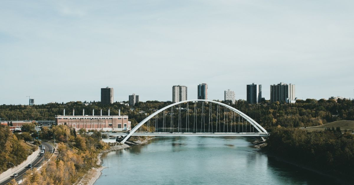 Edmonton Travel Guide: Planning Tips, Costs and Things to Do A contemporary cityscape with a modern bridge crossing a calm river, framed by high-rise buildings.