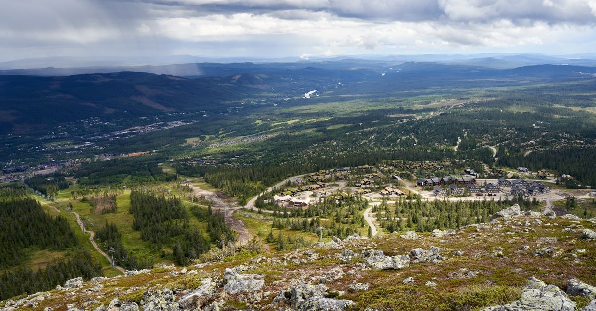 Edgewater Hotel, Whitehorse — A Yukon River Waterfront Landmark A breathtaking aerial view of a village nestled in a lush mountainous landscape under an overcast sky.