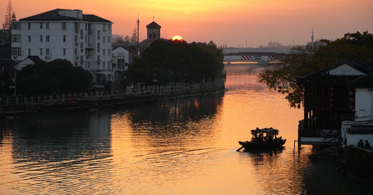 Suqian Travel Guide: A Quiet Canal City Worth Discovering Tranquil sunset scene with a traditional boat on a river in a Chinese town, capturing serenity.