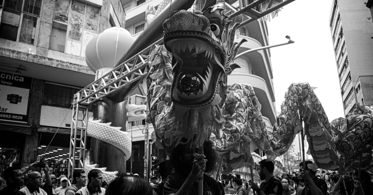Vibrant dragon dance performance during a street festival in a bustling urban setting, captured in black and white.