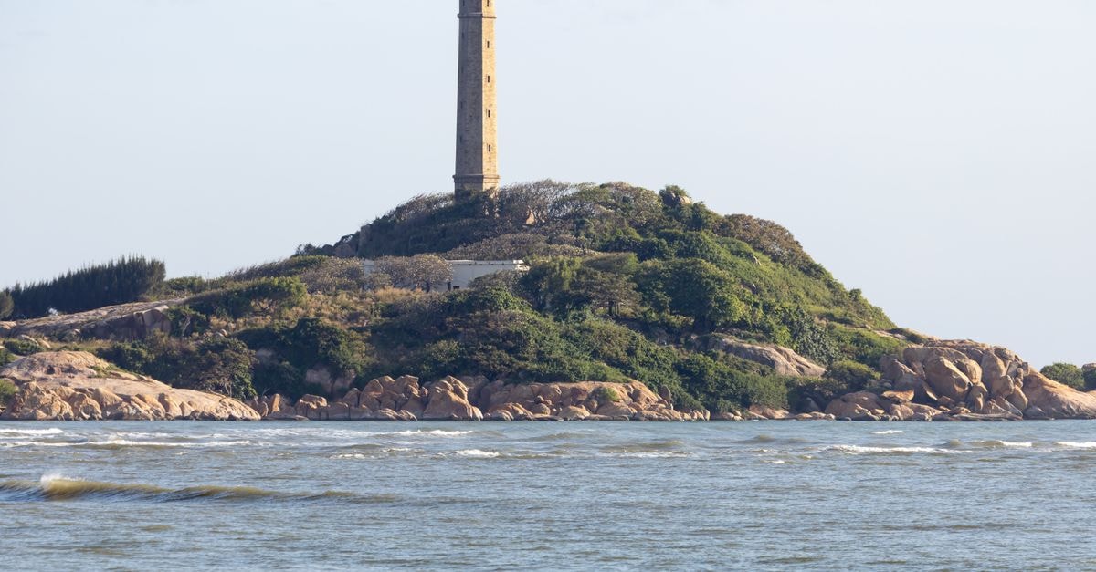 A lighthouse stands tall on a lush, rocky island surrounded by the serene ocean.