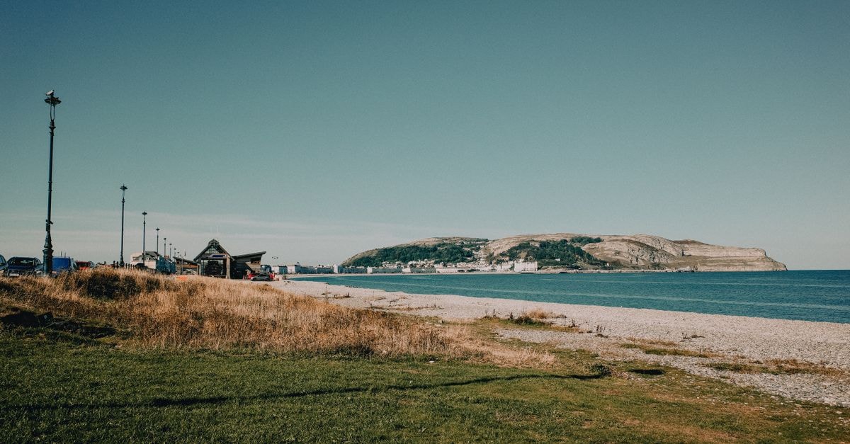 Swansea travel guide: a Welsh seaside city worth slowing down for Tranquil coastal landscape of Llandudno, Wales, showcasing grassy shores and distant Great Orme.