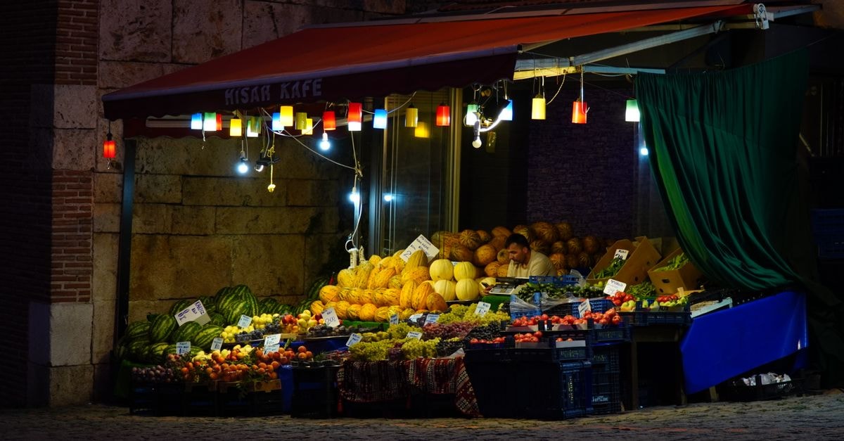 OYO Mid City Hotel in Hisar: A Sector 14 Stop on MDR107 Vibrant fruit stall under colorful lights at night, showcasing melons, tomatoes, and more.