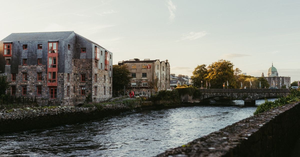 Eyre Square Hotel in Galway: City-Centre Base on Eyre Square Picturesque view of the river in Galway, Ireland at sunset with historic buildings and a charming bridge.