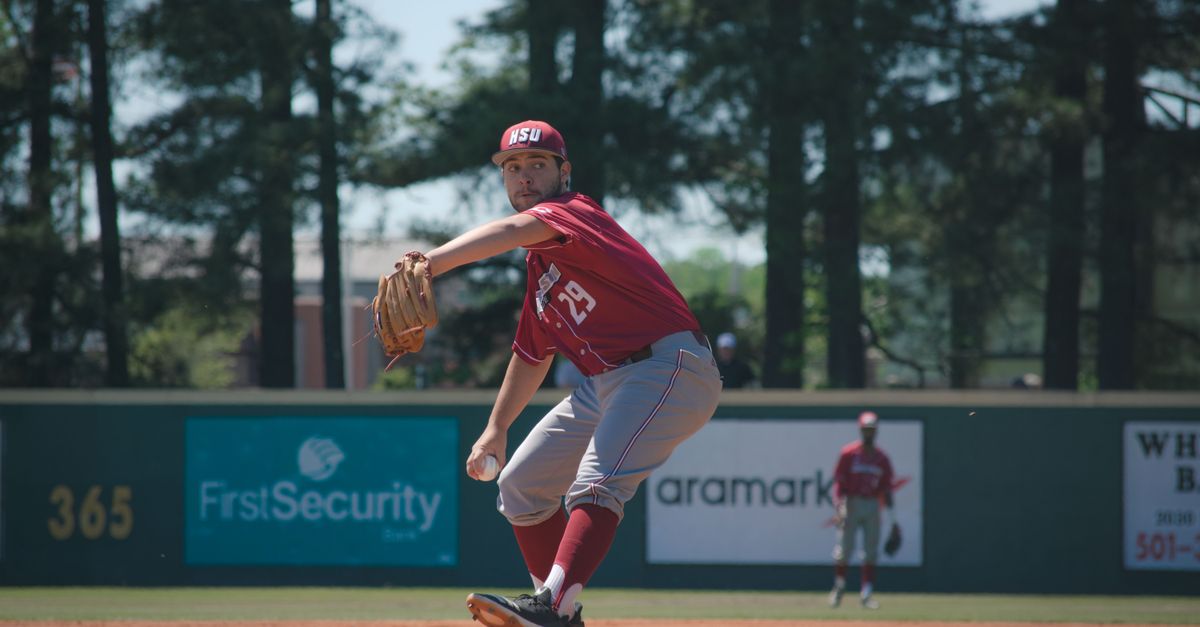 A focused baseball pitcher in red uniform prepares to throw on a sunny outdoor field.