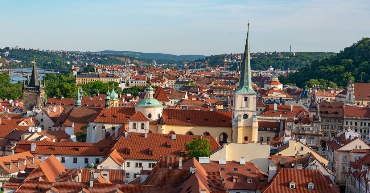 A Local-Style Prague Travel Guide: Things To Do, Eat, and Know Aerial view of Prague showcasing red rooftops and historic landmarks under a clear blue sky.