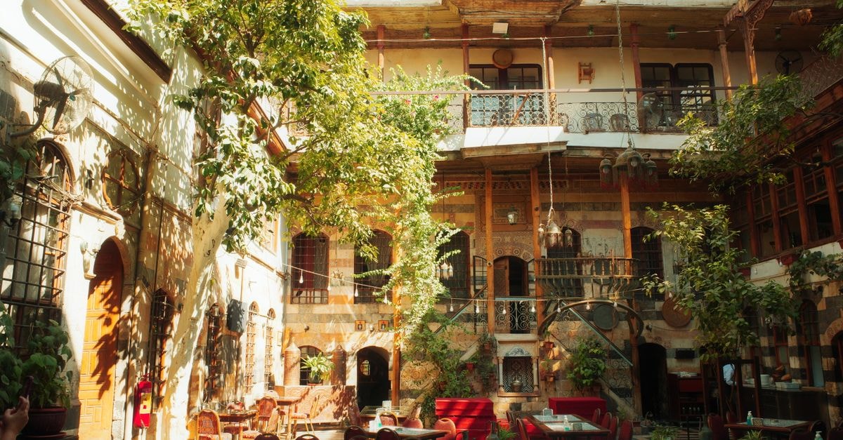 El Bayadh Travel Guide: Planning Tips, Costs and Things to Do Beautiful sunlit courtyard with traditional Mediterranean architecture and lush greenery.