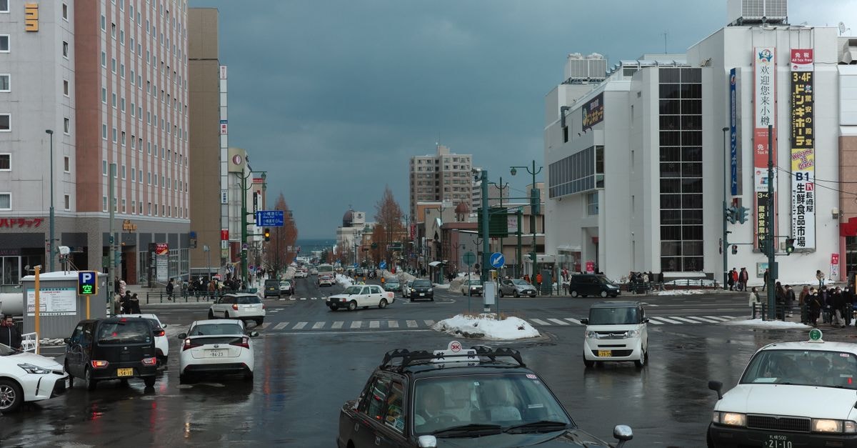 Daiwa Roynet Hotel Aomori in Aomori: Shinmachi 1-chome Address A busy winter street intersection in Otaru, Japan with cars and pedestrians on a cloudy day.