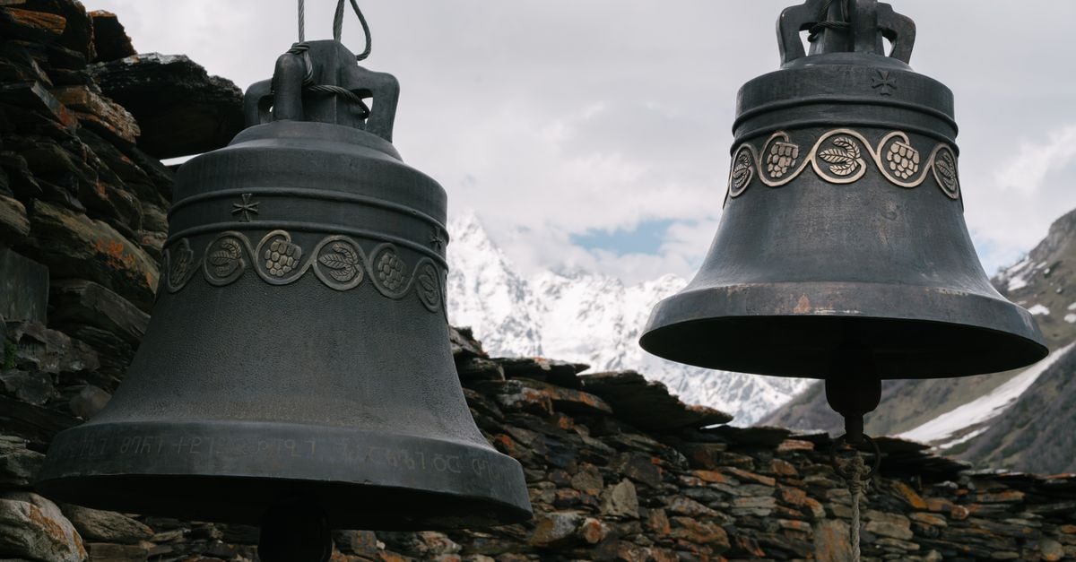 Aosta Travel Guide: Alpine Streets and Ancient Stones Close-up of ornate bells with a backdrop of snowy mountains and clouds.