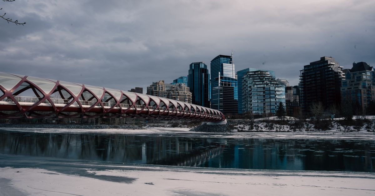 Scenic view of Calgary's Peace Bridge with city skyline and frozen river in winter.