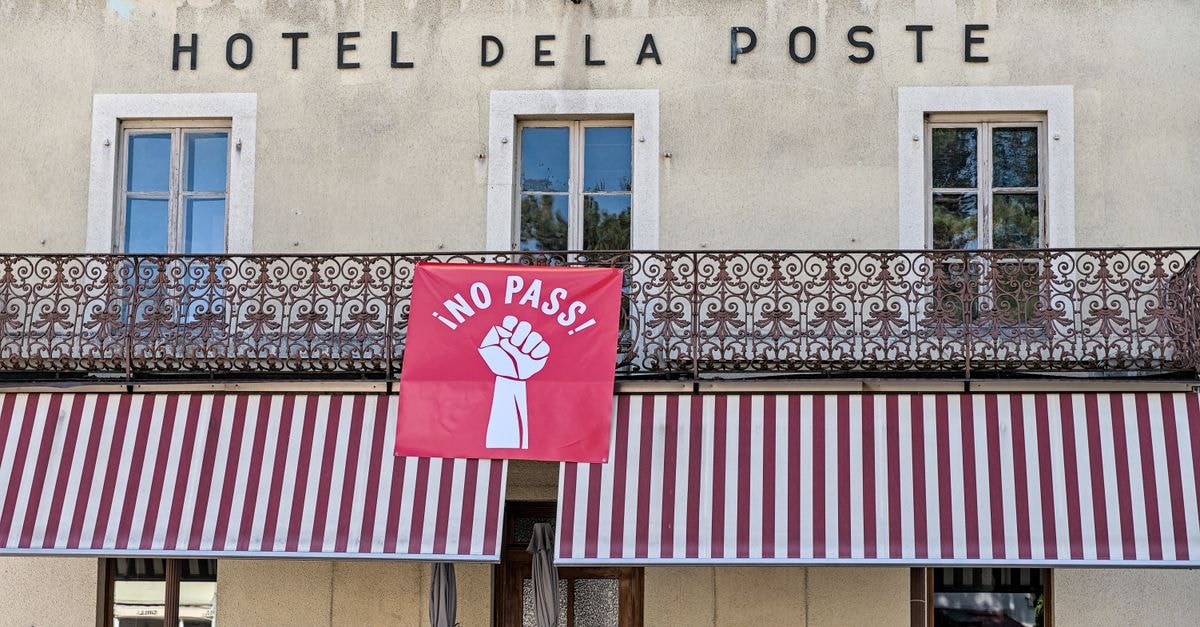 Hotel De La Poste facade with striking protest banner reading 'No Pass' in Val-de-Travers, Switzerland.