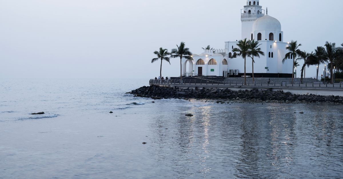 Jeddah Travel Guide: Red Sea Flavors and Easy City Moves Scenic view of a seaside mosque in Jeddah, Saudi Arabia with palm trees and calm waters.