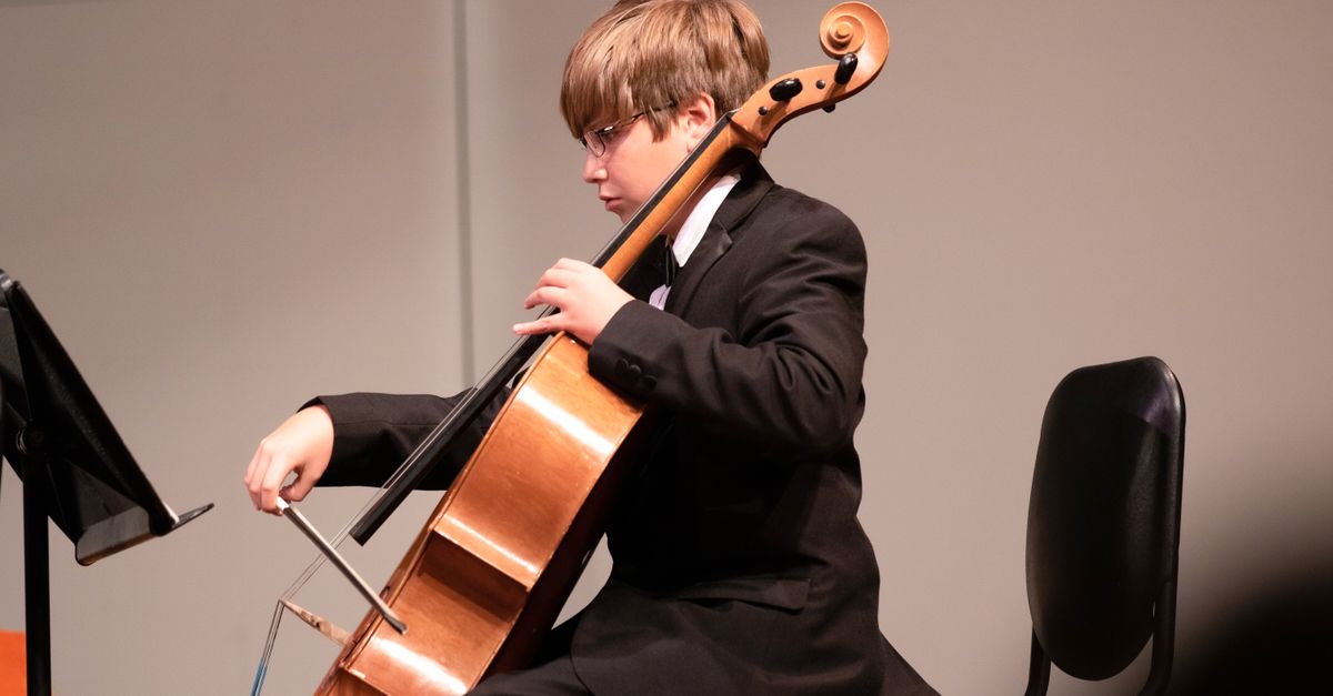 A young boy in a suit plays the cello during an indoor classical music performance.